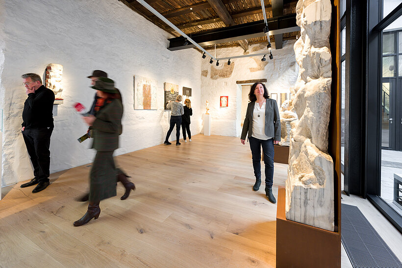 Museum Karlstadt/Foto: Jürgen Müller Menschen im Museum, die Bilder, die an einer weißen Wand hängen und Skulpturen betrachten.
