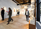 Menschen im Museum, die Bilder, die an einer weißen Wand hängen  und Skulpturen betrachten.