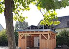 Holzhäuschen mit Solarpaneelen auf dem Dach und Karte im Häuschen, Baum davor