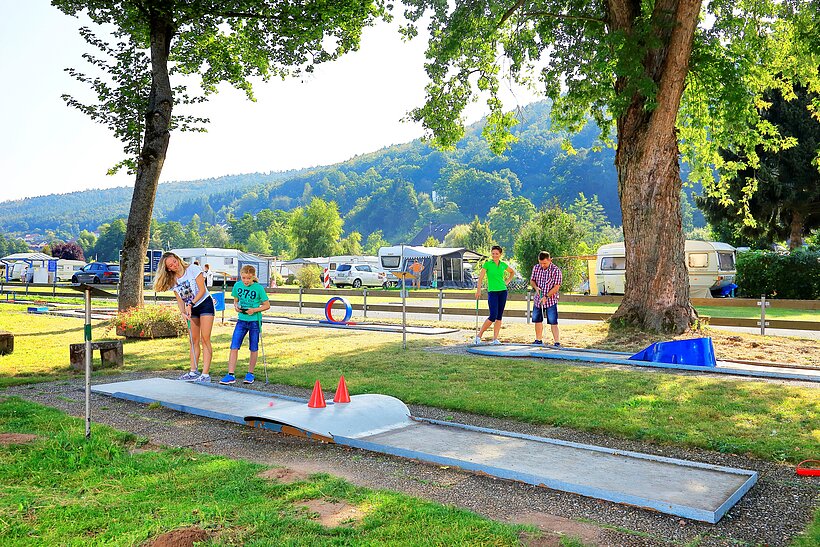 Minigolfstation am Platz mit spielenden Besuchern inmitten von Bäumen