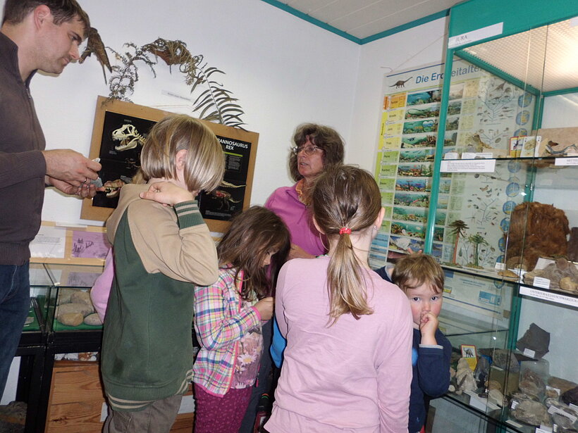 Raum mit Glasvitrinen, bestückt mit Steinen und Fossilien, eine Kindergruppe steht um einen Tisch