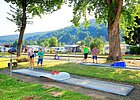Minigolfstation am Platz mit spielenden Besuchern inmitten von Bäumen
