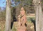 Zwischen zwei Bäumen steht eine rote Sandsteinfigur