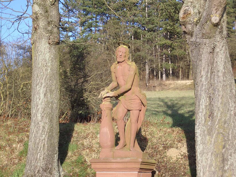 Eußenheim Bildstock Aschfeld Foto: Fr. R. Zöller Zwischen zwei Bäumen steht eine rote Sandsteinfigur