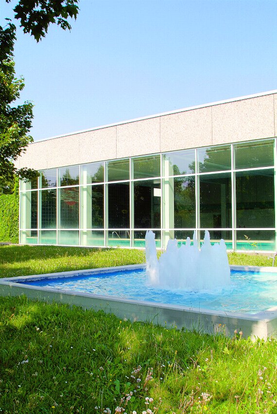 Werneck Schwimmbad Außenaufnahme: Gebäude mit Glasfront, grünem Rasen davor und kleinem Becken mit Springbrunnen in der Mitte