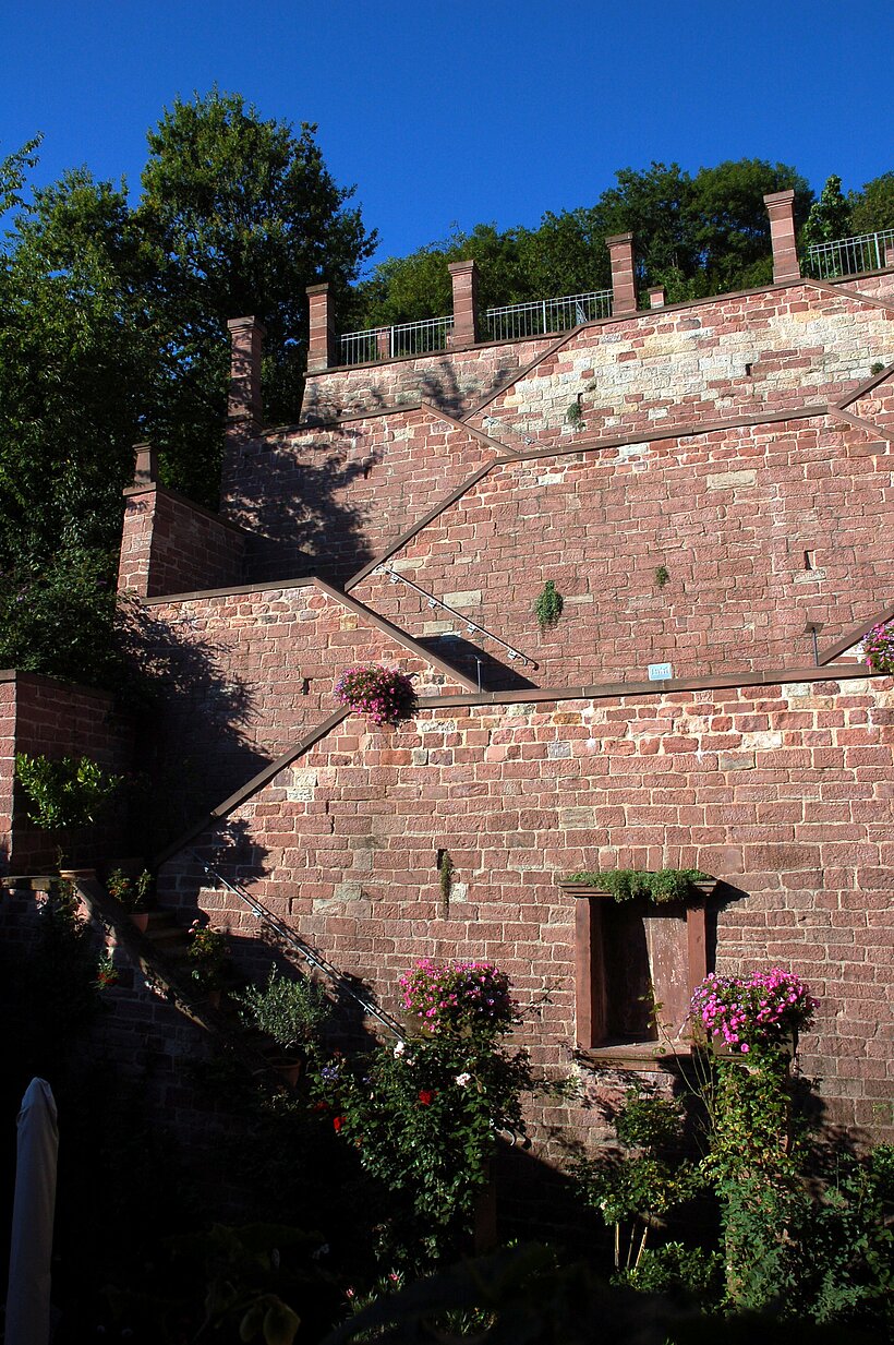 Ronkarzgarten Gemünden a.Main Hohe rote Sandsteinmauer, unterbrochen durch nicht sichtbare Treppe, links umringt von Bäumen und Sträuchern