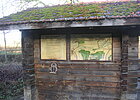 Holzhütte mit Karte an der Außenfassade, auf dem Dach wächst Moos