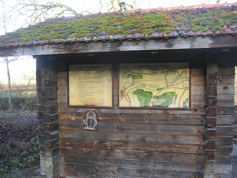 Holzhütte mit Karte an der Außenfassade, auf dem Dach wächst Moos