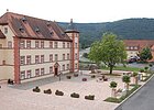 Platz mit Baum in der Mitte, daneben links dreigeschossiges Haus