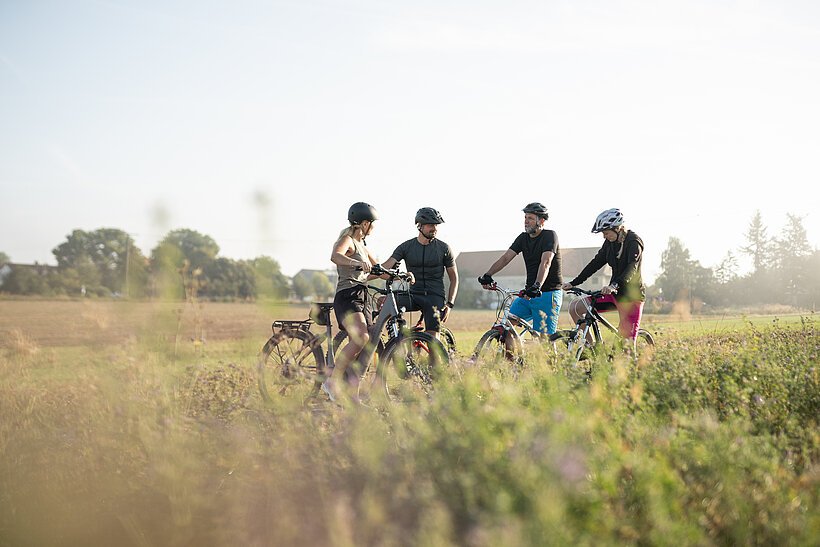 Vier Radfahrer und Radfahrerinnen stehen mit ihren R&auml;dern auf einem Weg und machen eine kurze Pause