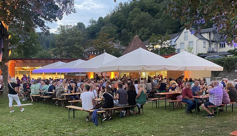 Festplatz im Gr&uuml;nen mit Tischen, Sonnenschirme und viele Personen