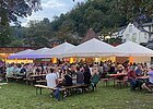 Festplatz im Gr&uuml;nen mit Tischen, Sonnenschirme und viele Personen