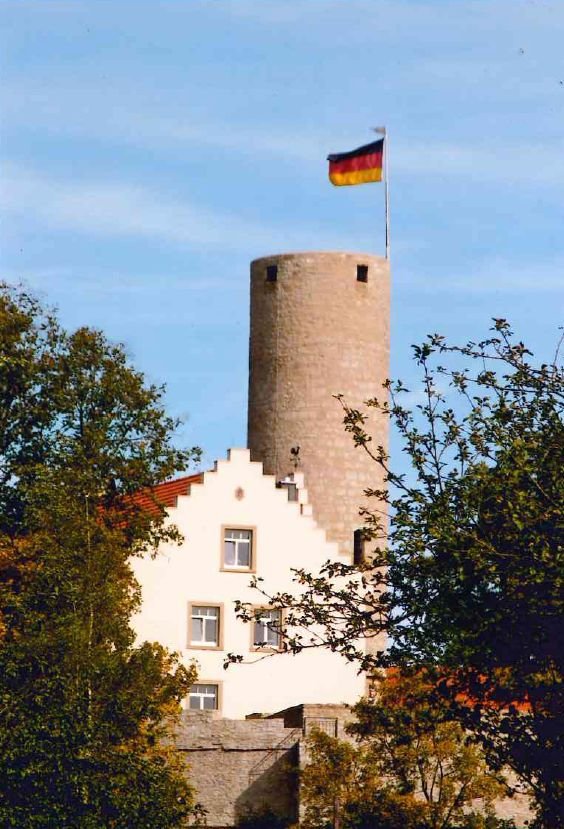Arnstein Schloss Büchold Weiße Giebelfassade mit kleinen Zinnen, Steinturm mit Fahne daneben, rechts und links zwei Bäume