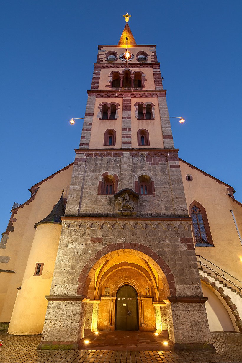 St. Andreas Karlstadt/Jochen Schreiner Kirchenfassade mit Turm, Eingang unter Turm, beleuchtet in Abenddämmerung